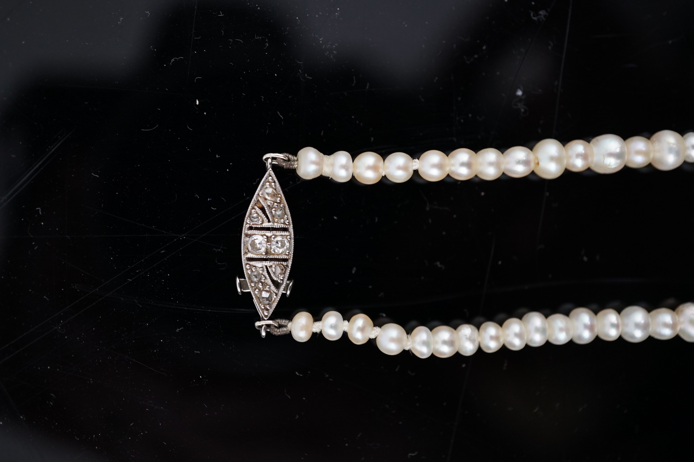 A late 19th century single strand graduated natural saltwater pearl necklace, with a French 18ct white gold and millegrain set diamond marquise shaped clasp